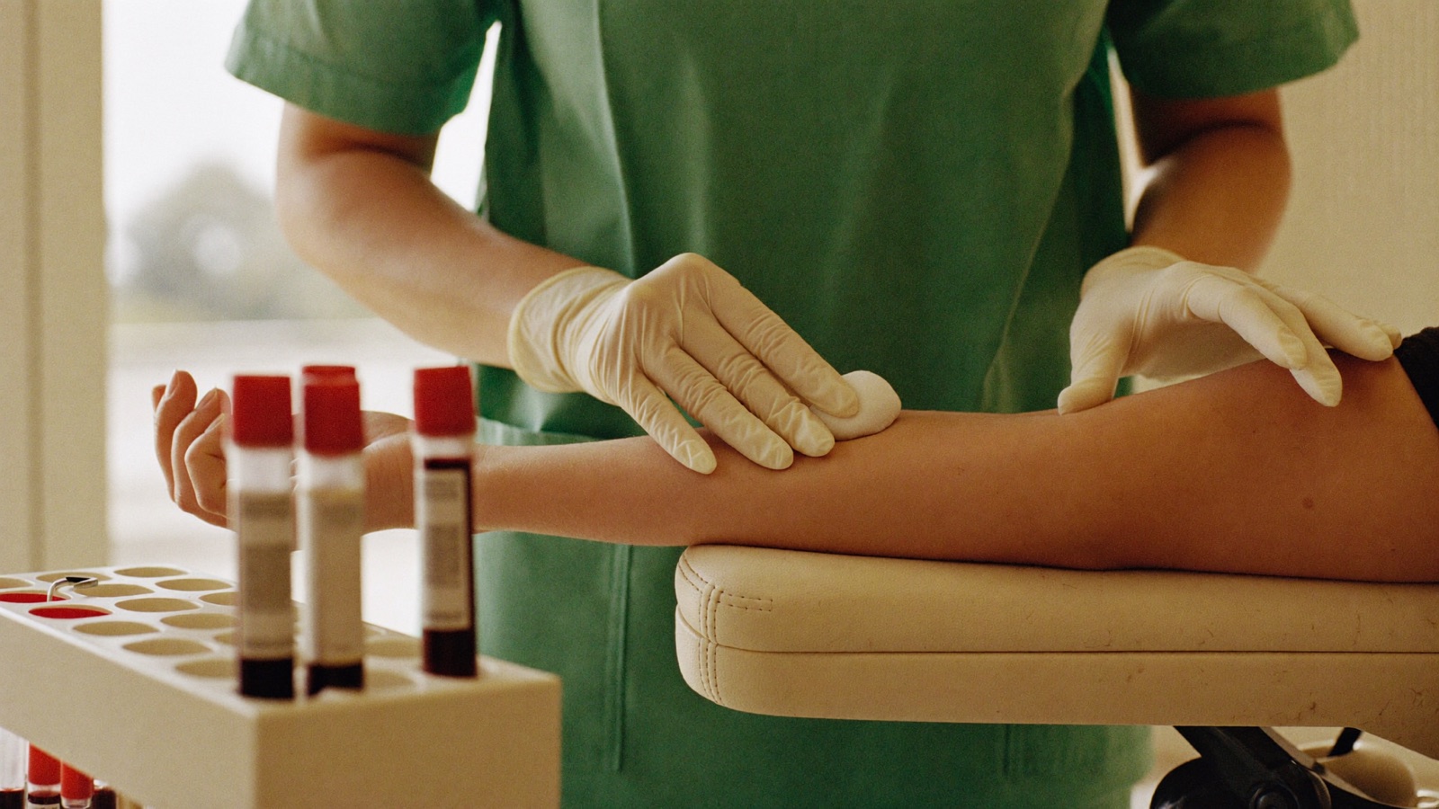 Profissional aplicando curativo após coleta de sangue, com tubos de amostra em primeiro plano